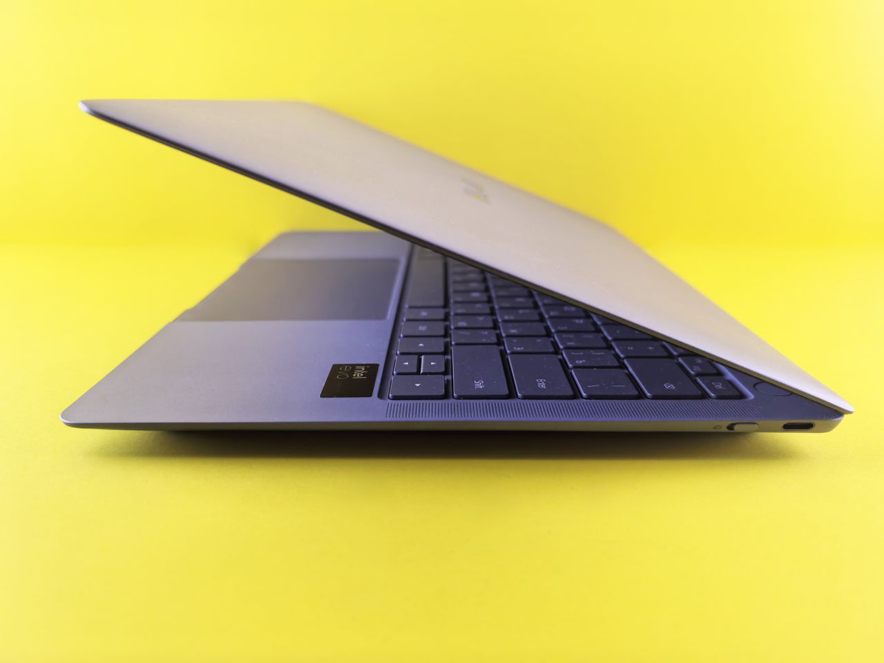 Modern laptop partially closed against a bold yellow backdrop, showcasing sleek design.