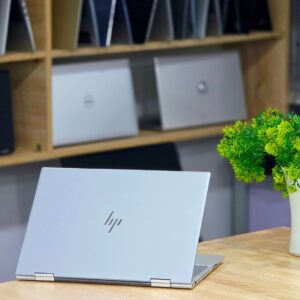 Open laptop on a wooden desk with a plant, conveying a modern and professional workspace.